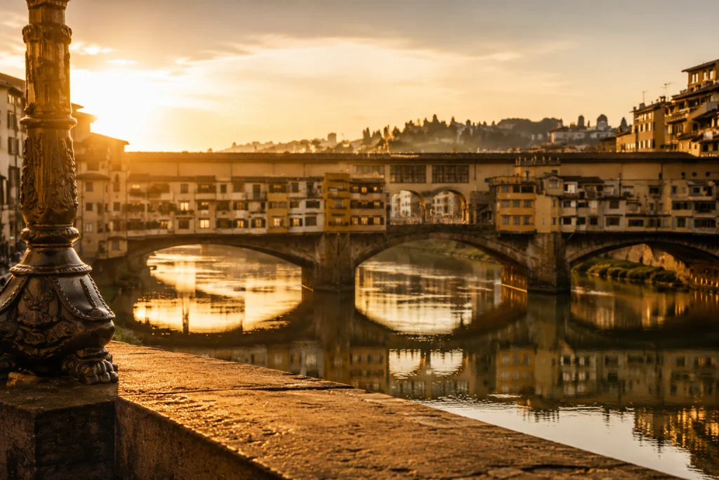 Vista romantica del Ponte Vecchio a Firenze al tramonto con luce dorata sul fiume Arno e architettura rinascimentale in stile fotografico editoriale elegante e senza persone.